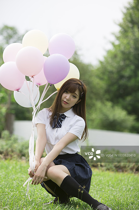 年轻美丽的女孩在公园的草地上拿着彩色的气球。图片素材