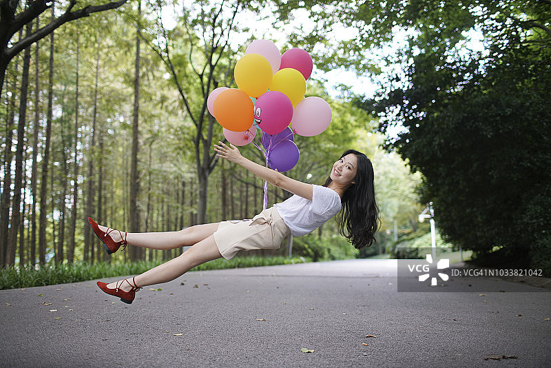 美丽的亚洲女人在公园里被一堆气球举起来图片素材
