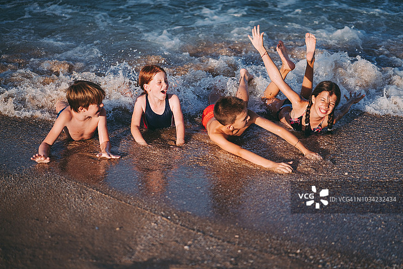 四个快乐的孩子躺在沙滩上图片素材