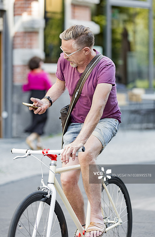 60岁出头的活跃老人用手机享受夏季的城市生活。图片素材