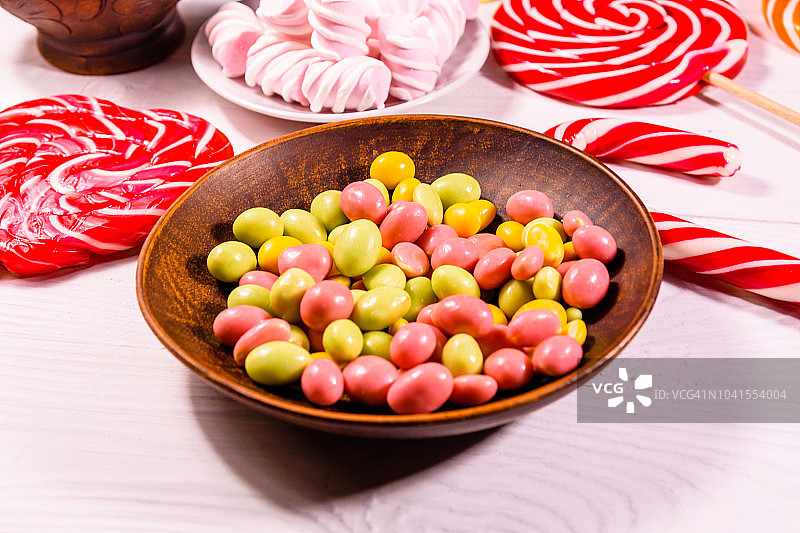 瓷盘，木桌上放着彩色糖果、拐杖糖、棒棒糖和棉花糖图片素材