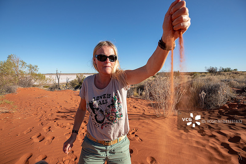 金发女人让红色的澳大利亚沙子从她的手在沙漠图片素材