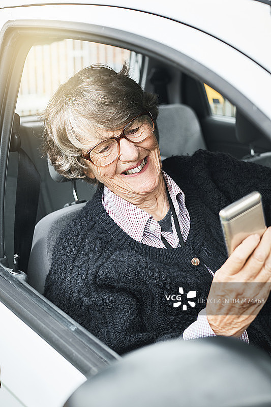 微笑的年长妇女在车看智能手机图片素材