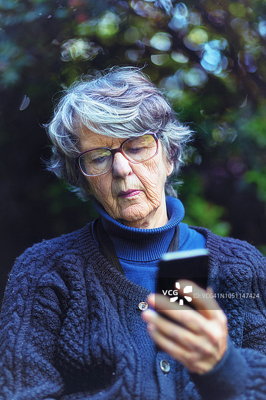 花园里的老妇人低头看手机短信图片素材