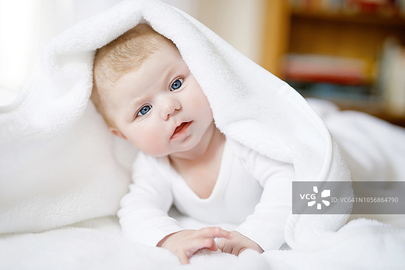 女婴穿着白色的毛巾或冬季工作服在白色的阳光卧室里图片素材