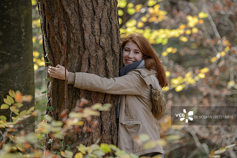 在秋天的森林里，快乐的少女抱着树干的肖像图片素材