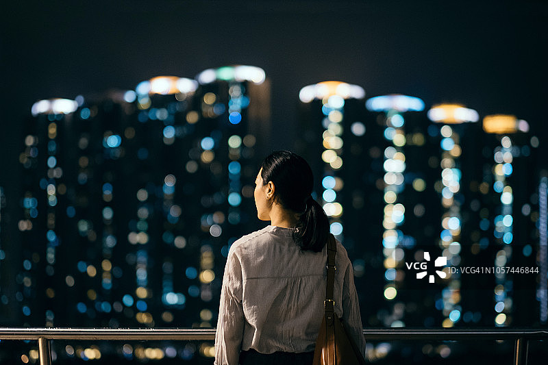 女人的后视图俯瞰香港的城市景观在晚上的码头图片素材