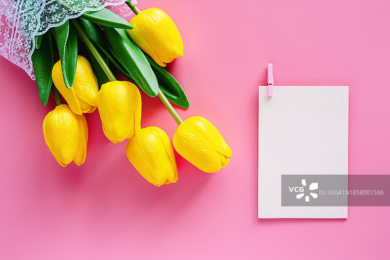 人工黄色郁金香与白色纸卡在粉红色的背景，自然装饰和春天的概念图片素材