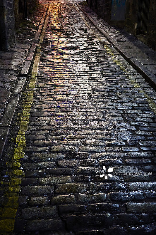 爱丁堡老城区，老式的石头铺成的道路在晚上被雨水淋湿，反射着街灯图片素材