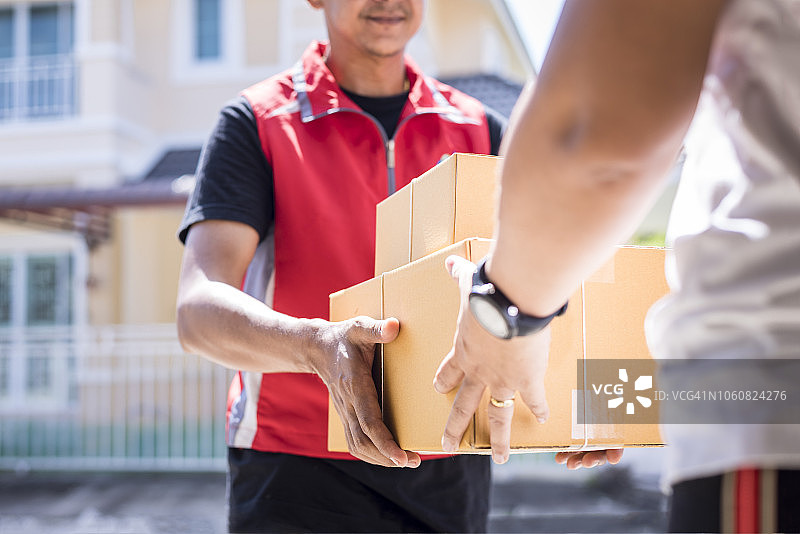 包裹快递员通过服务和客户的手接受快递员交付的盒子。图片素材