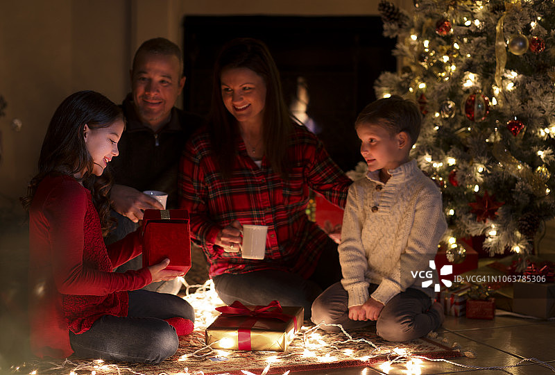 圣诞节期间，一家人在树旁打开礼物。图片素材