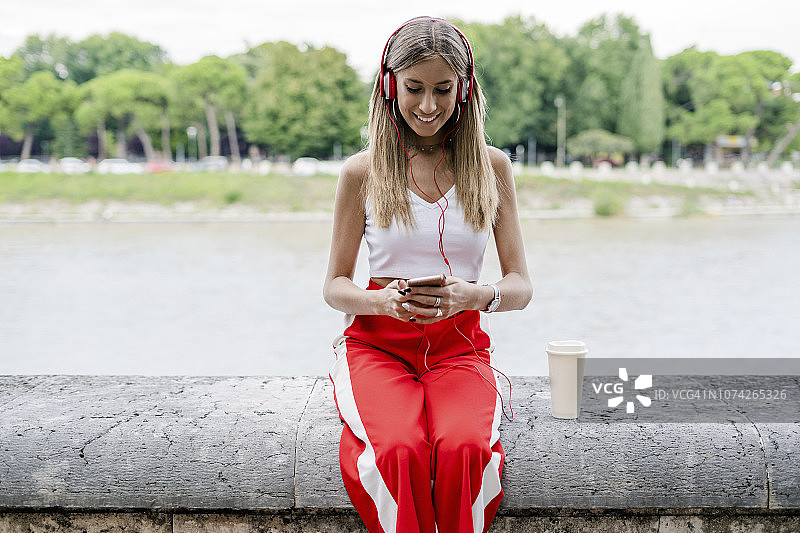 微笑的少女戴着耳机和使用手机在河边图片素材