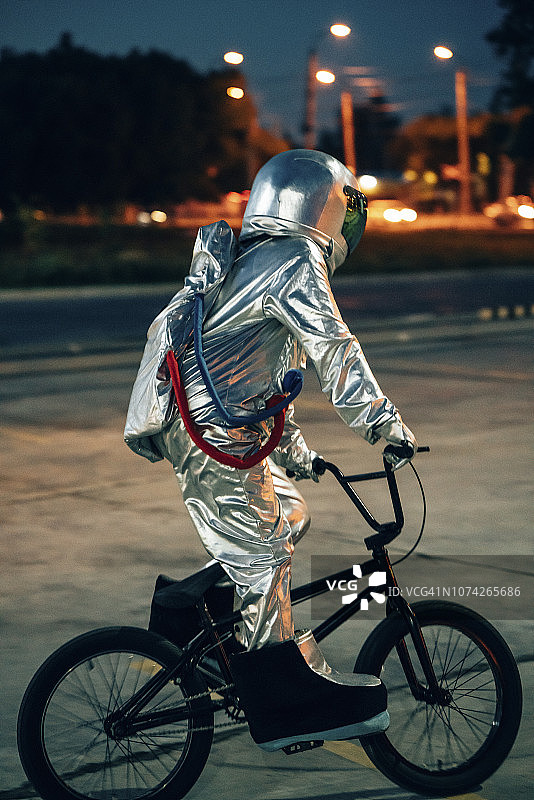 宇航员晚上在城市的停车场上骑小轮车图片素材