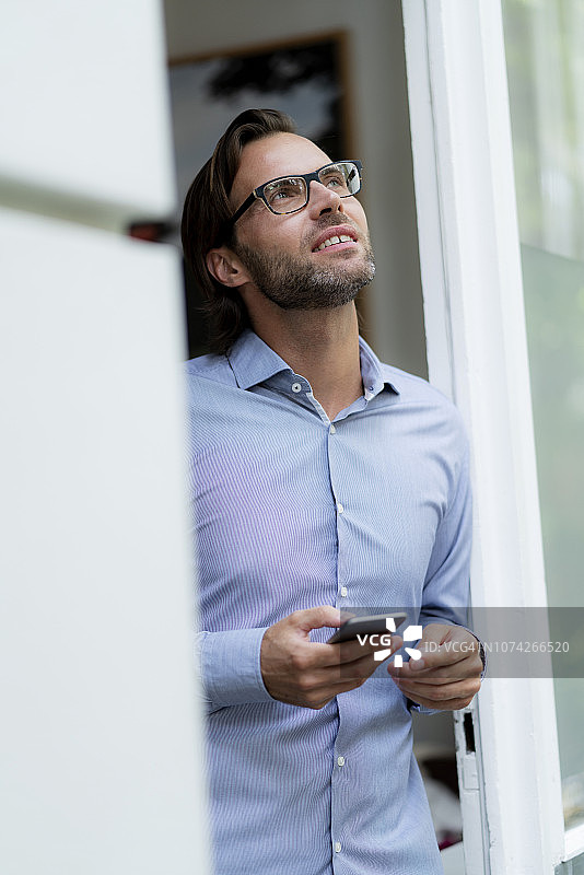 一个自信的男人站在门框里拿着手机抬头看图片素材