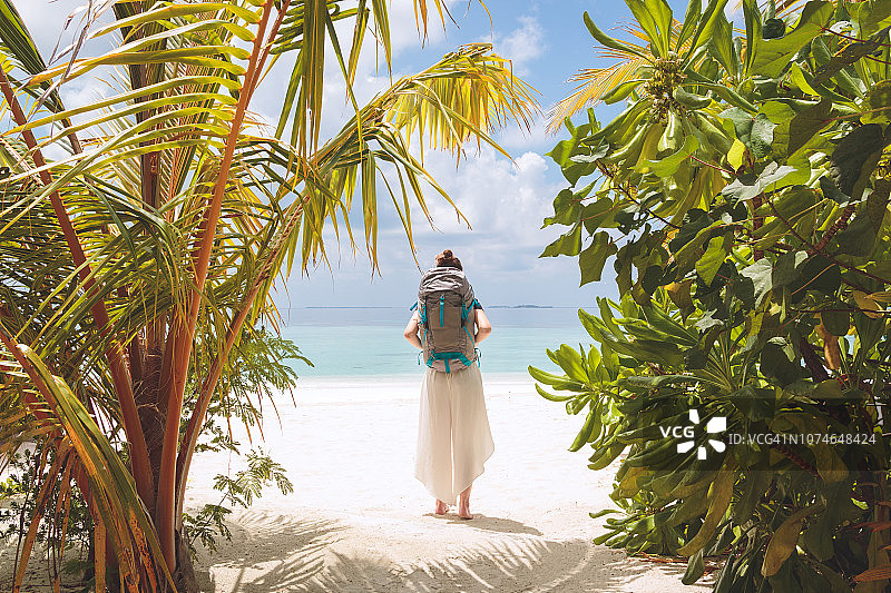 年轻女子背着大背包走到一个热带度假目的地的海滩图片素材