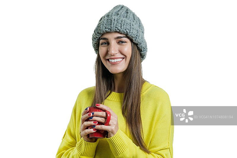 肖像微笑的冬天年轻女子在编织的帽子，黄色毛衣与杯热饮料，孤立的白色图片素材
