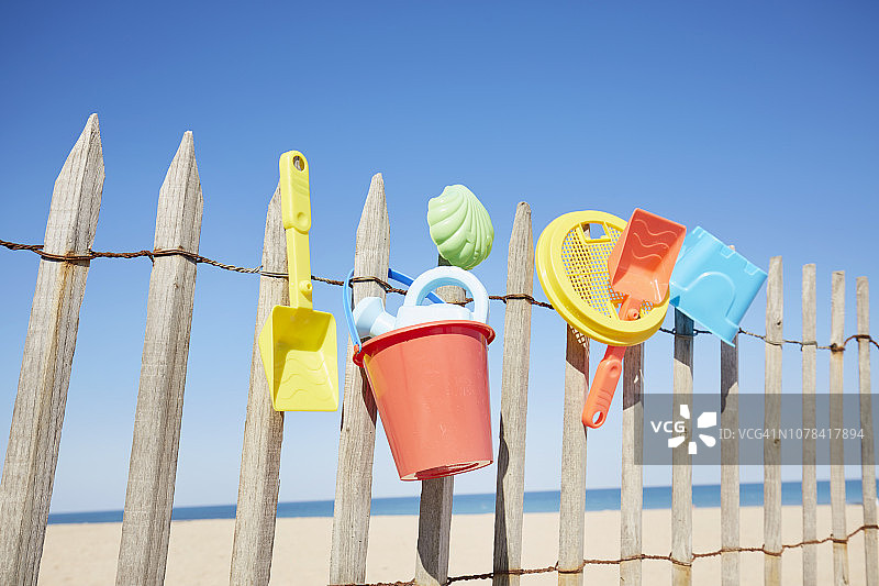 色彩丰富的沙玩具静物画，挂在沙滩的木栅栏上，对着大海和蓝天图片素材