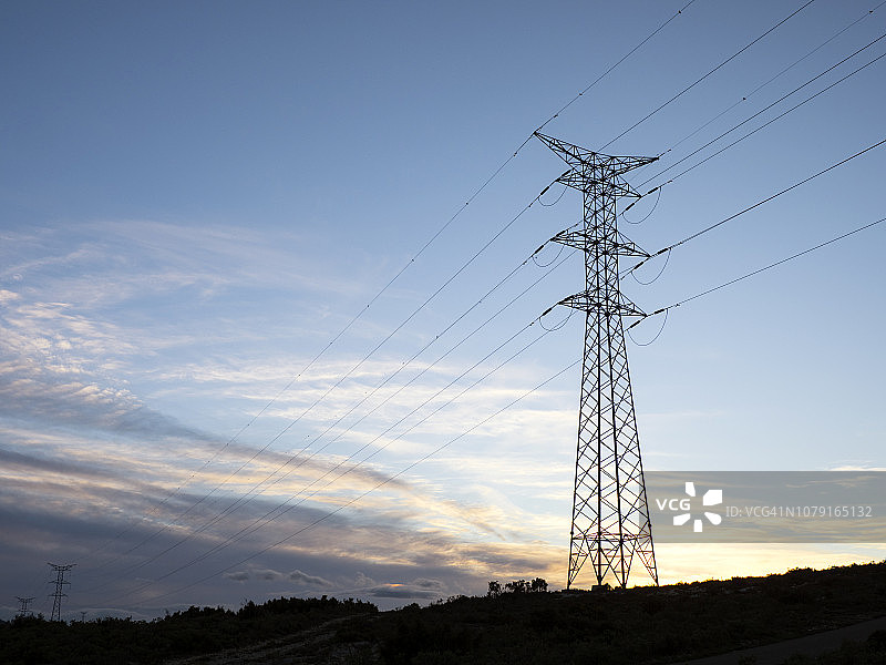 高压大电塔用于在日落时分在山上分配电力。图片素材