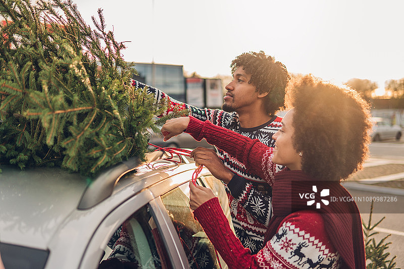 一对夫妇把圣诞树绑在车顶上图片素材