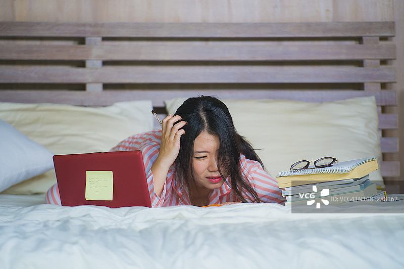 年轻沮丧和疲惫的亚洲韩国大学生女孩感到不堪重负和压力准备考试学习与笔记本电脑在压力和在家床上过度工作图片素材