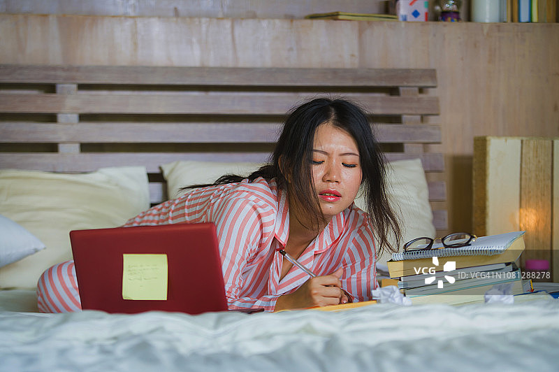年轻沮丧和疲惫的亚洲中国大学生女孩感到不堪重负和压力准备考试学习与笔记本电脑在压力和在家床上过度工作图片素材