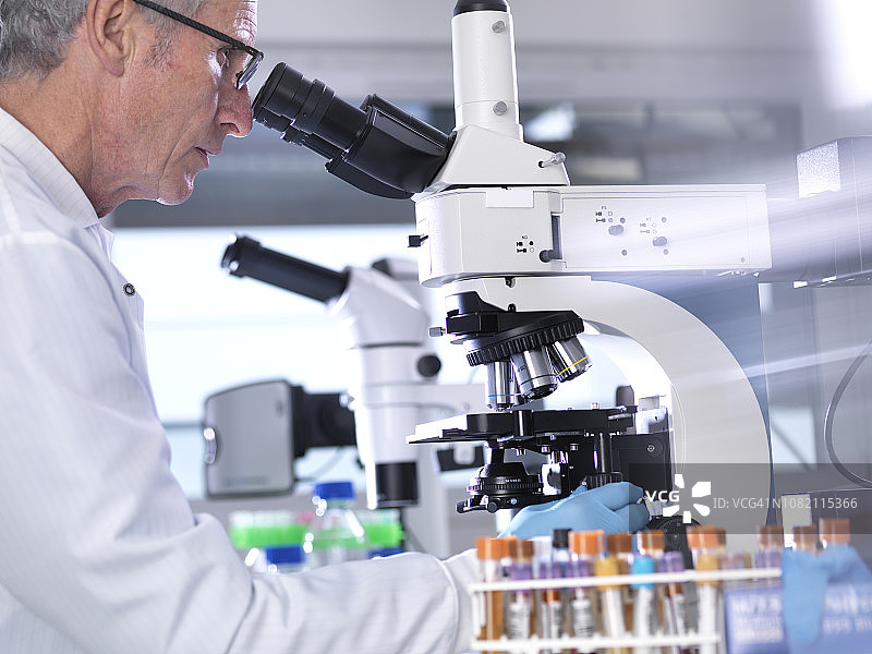 在实验室通过显微镜分析血液样本的男性科学家的侧视图图片素材