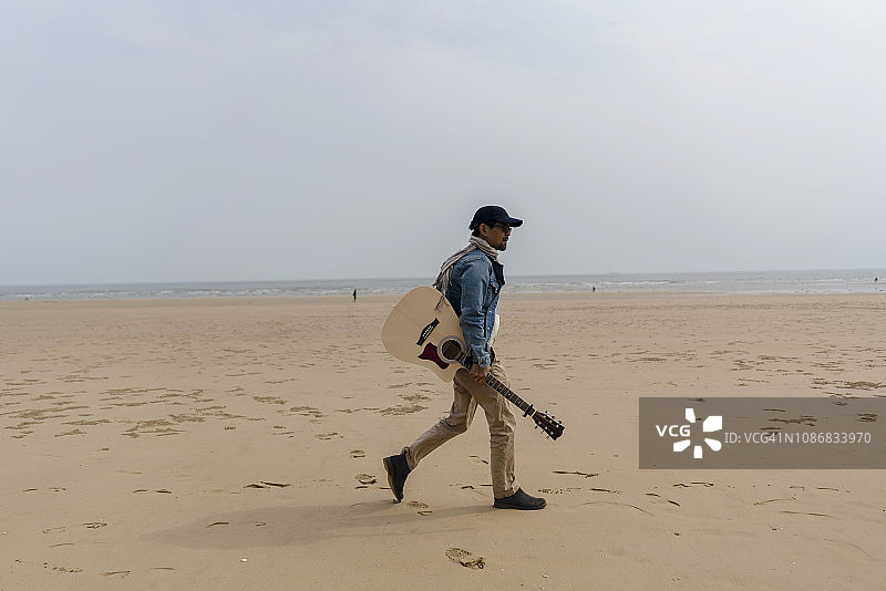 一个人拿着吉他走在海滩上图片素材