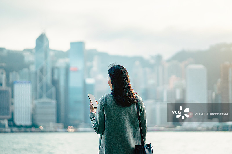 年轻的职业女商人在市中心使用智能手机，在现代城市的天际线前图片素材