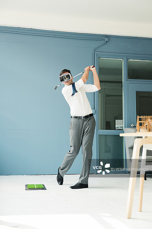 商人戴着VR眼镜在办公室打高尔夫图片素材