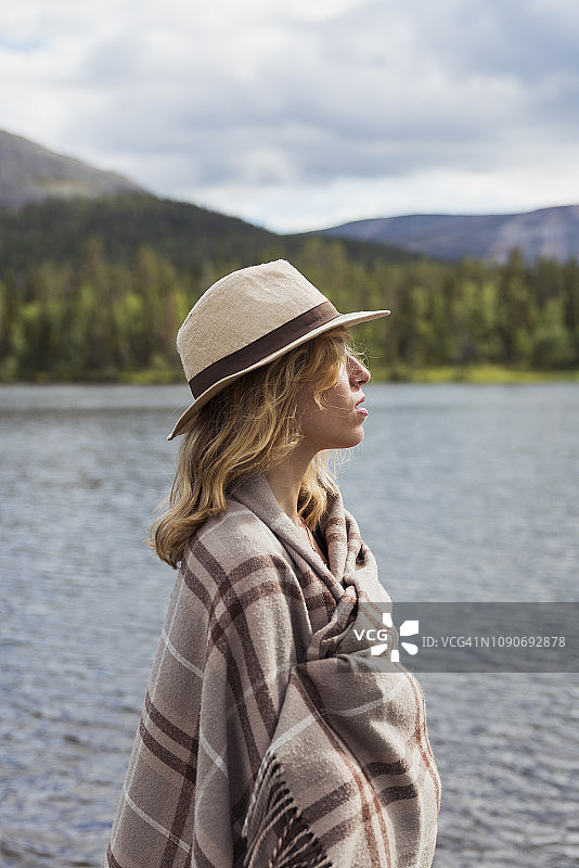 芬兰，拉普兰，一个戴着帽子裹着毯子的女人站在湖边图片素材