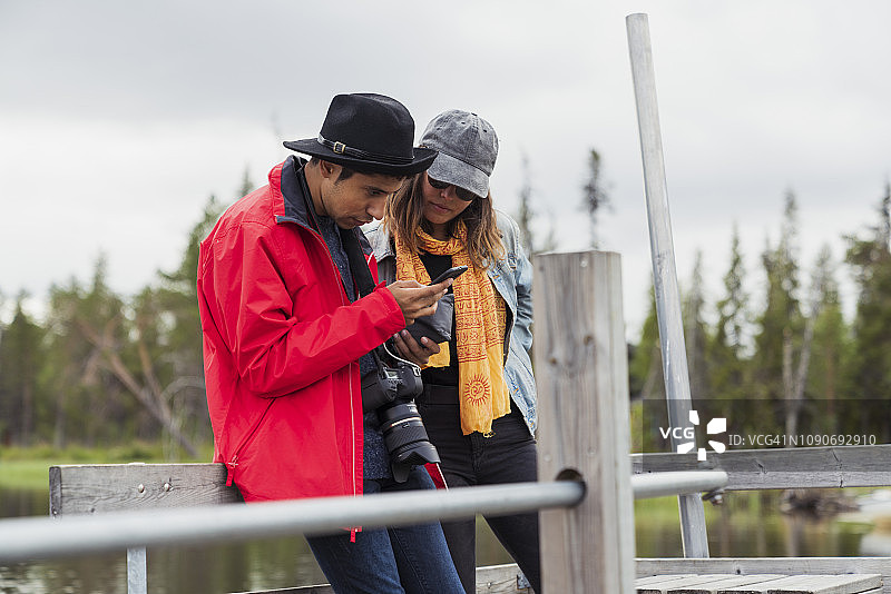 芬兰，拉普兰，一对夫妇在湖边的码头上使用手机图片素材
