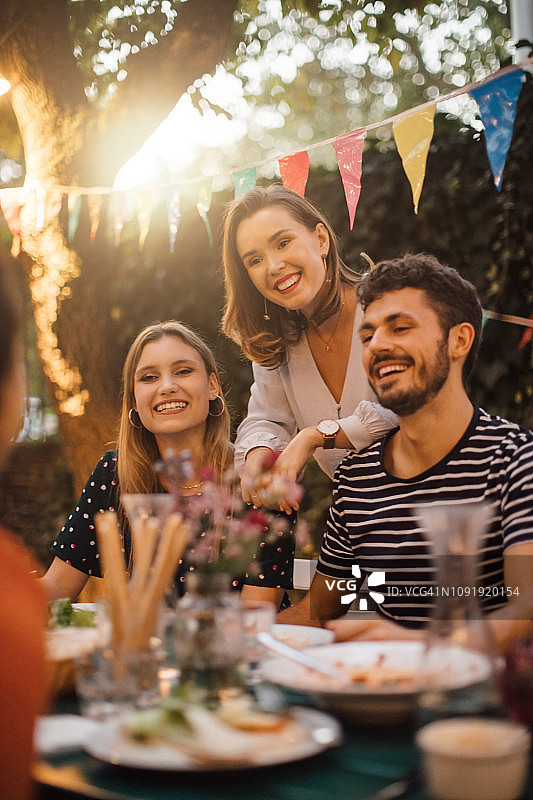 快乐的年轻男性和女性朋友在餐桌上在后院的晚餐聚会图片素材