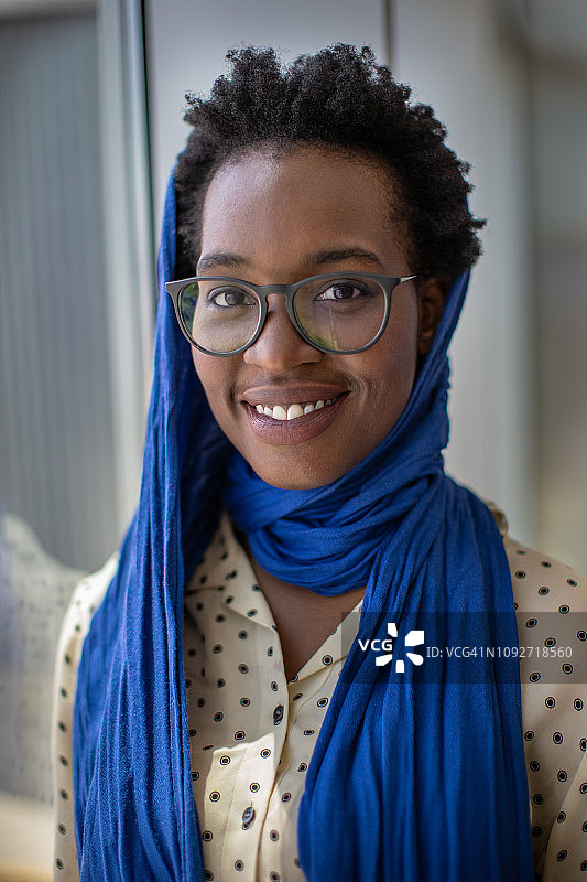 年轻的非洲裔美国妇女戴着眼镜，围着围巾，对着镜头微笑。图片素材