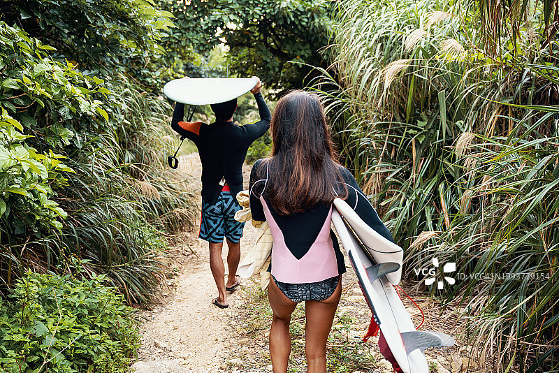 一对成熟的夫妇带着冲浪板穿过茂密的丛林植被图片素材