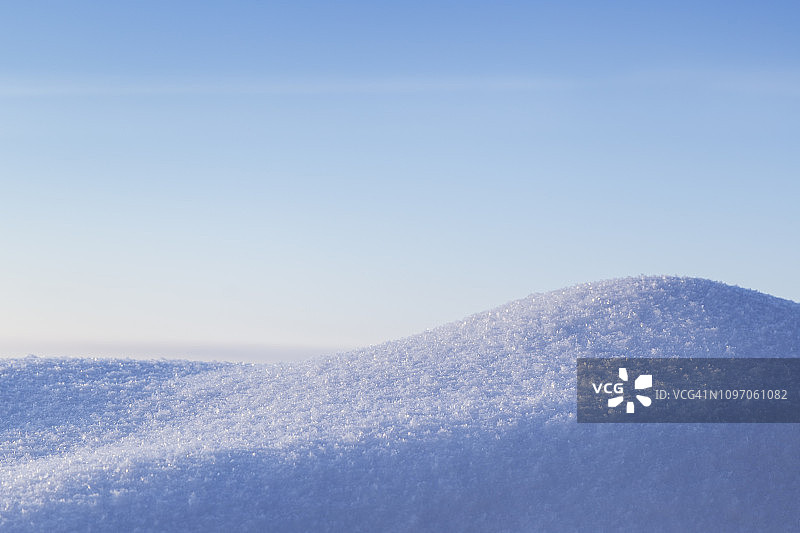 在一个阳光明媚的日子里，在一个雪堆上的新鲜闪亮的雪的特写。晴朗的蓝天，复制空间。图片素材