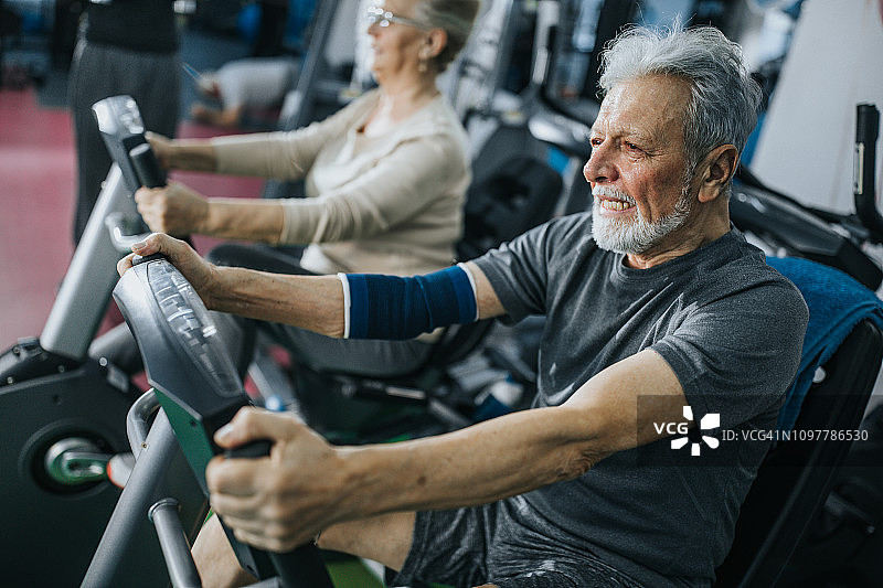 大汗淋漓的老人正在健身房里的自行车上进行运动训练。图片素材