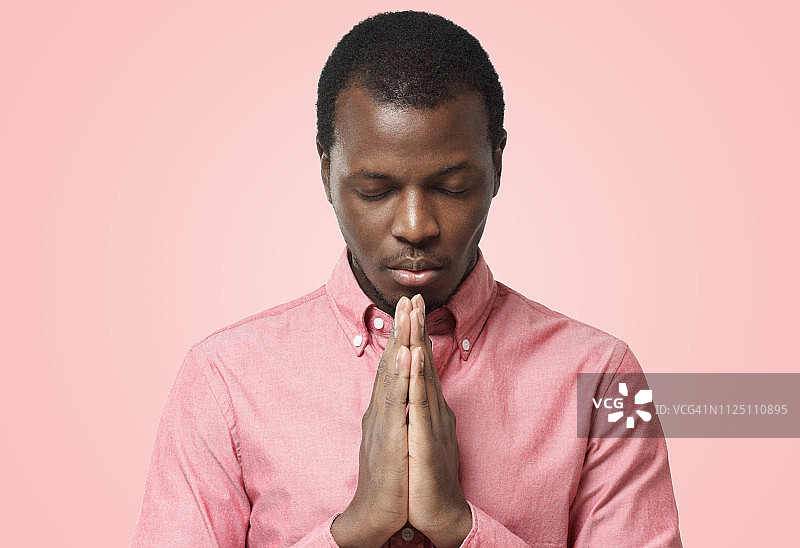 年轻的非洲裔美国人闭上眼睛祈祷的特写，孤立的粉红色图片素材