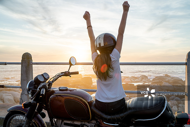 年轻女孩坐在复古摩托车上用手臂展示胜利图片素材