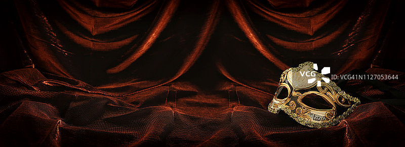 照片优雅和精致的金色威尼斯面具在黑暗的天鹅绒和丝绸背景。图片素材