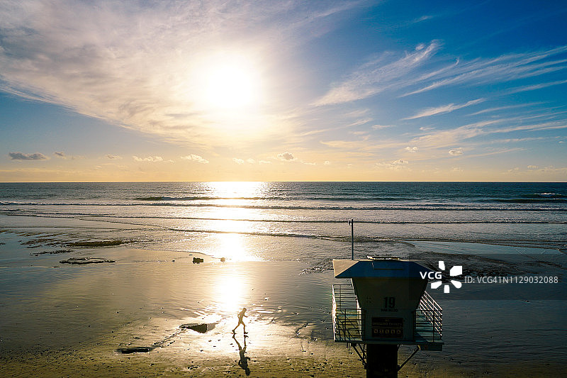 救生员塔和日落时海滩上奔跑的男子剪影。图片素材