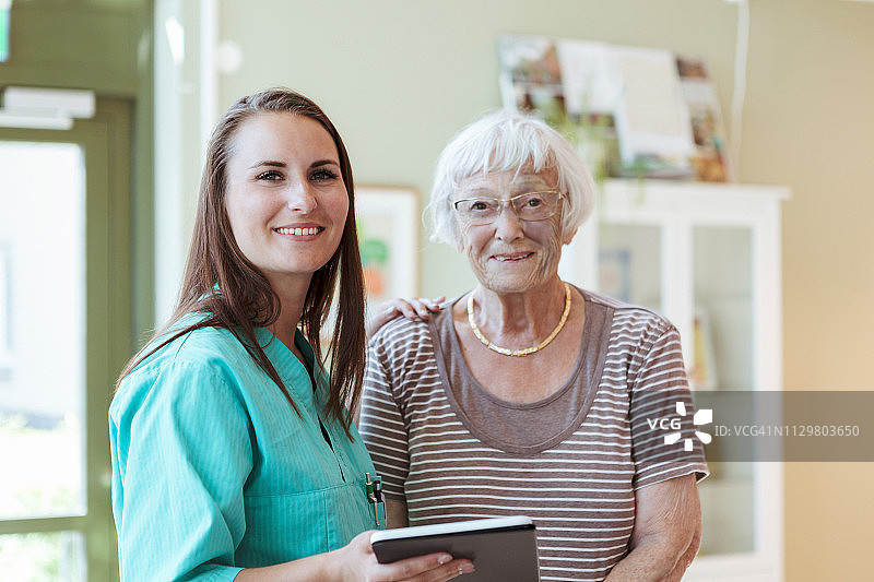 微笑的老年妇女和护士的肖像与数字平板电脑在家里图片素材