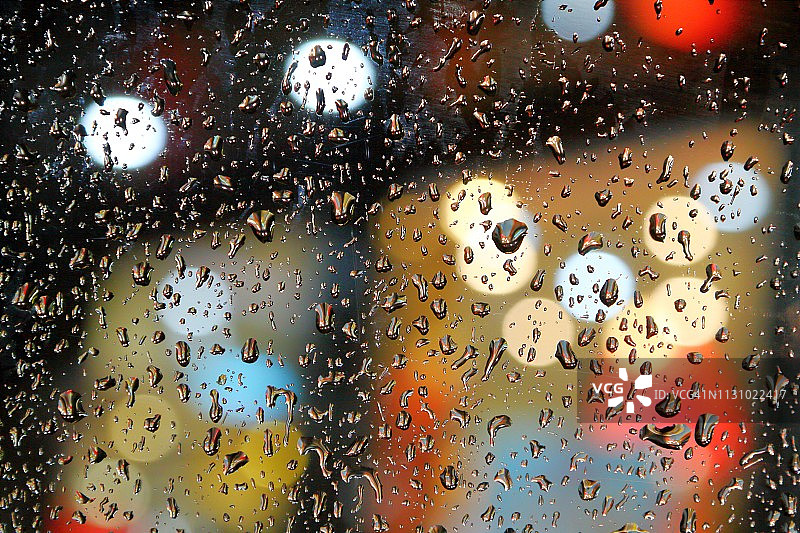 雨滴落在窗户玻璃上，使背景中的彩色灯光散焦图片素材
