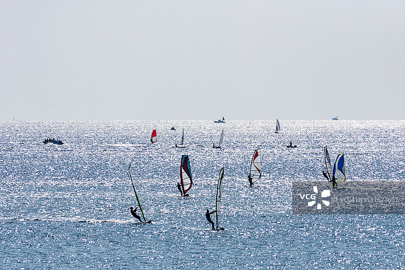 在日本神奈川县藤泽市的阳光海滩上，风帆冲浪者和帆船爱好者在享受图片素材