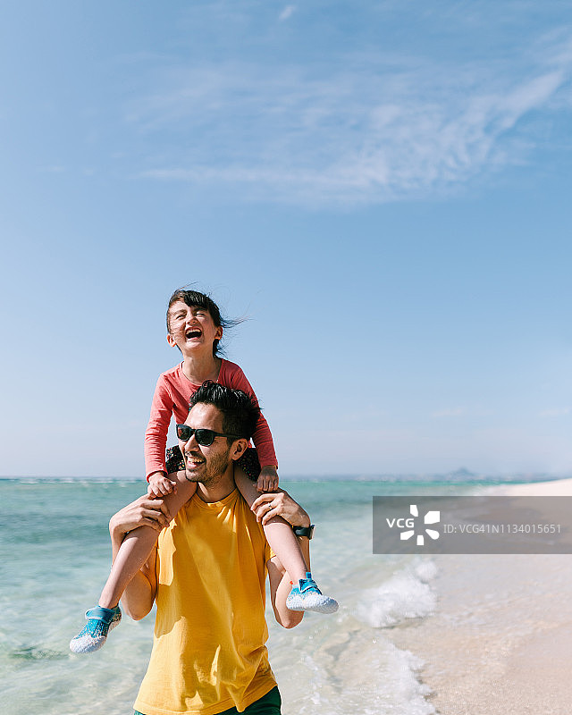 小女孩喜欢骑在父亲背上在热带海滩，冲绳，日本图片素材