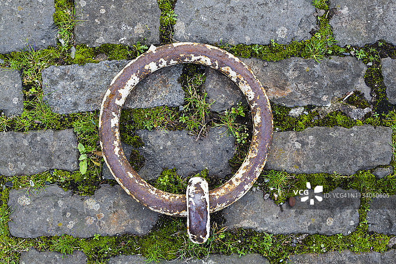 在一个废弃的码头边，鹅卵石上的一个生锈的金属系泊环图片素材