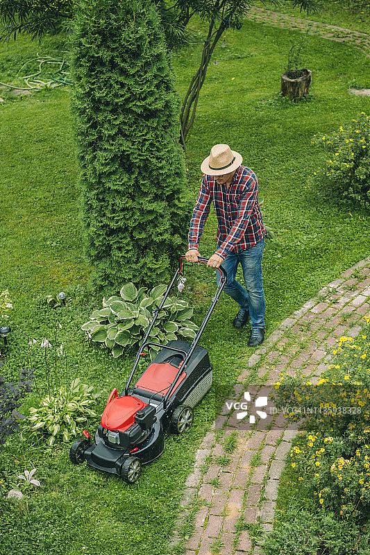 一个男人在后院用割草机割草图片素材