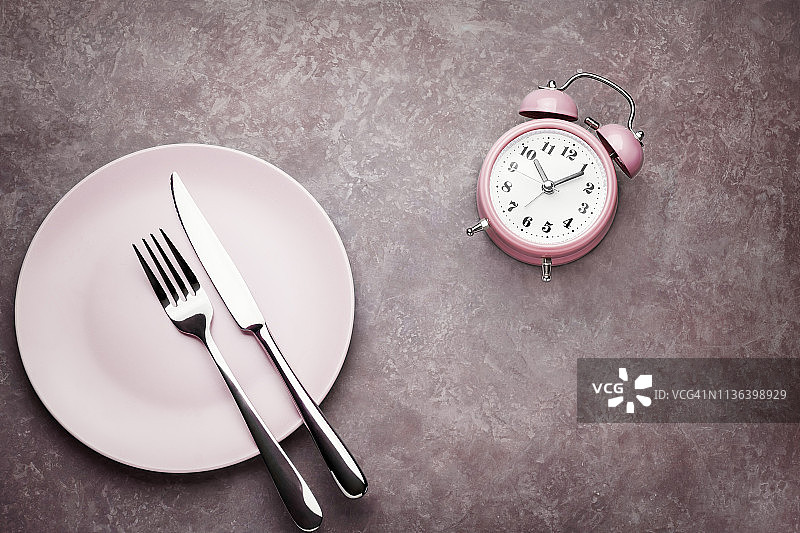 闹钟和带有餐具的盘子。间歇性禁食、午餐、饮食和减肥的概念图片素材