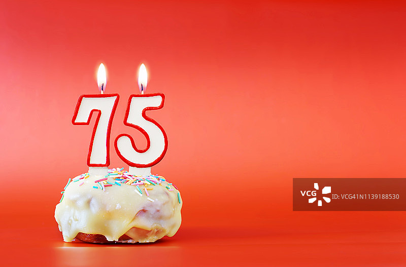 七十五岁生日。75号白色蜡烛纸杯蛋糕。鲜艳的红色背景与复制空间图片素材