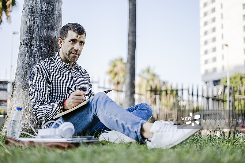 一个坐在草地上记笔记的男人的肖像图片素材