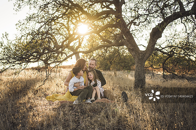 一家人依偎在加州田野树下的毯子上图片素材